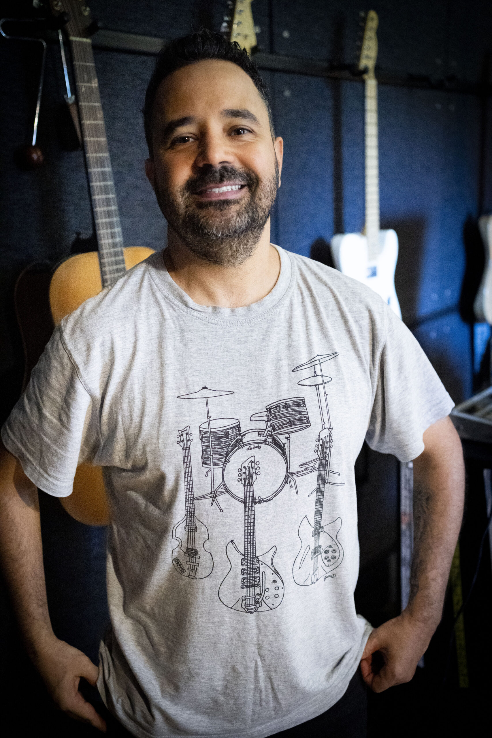 Man standing in a studio, guitars and music equipment in the background.