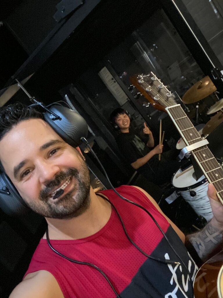 Music teacher smiling in the studio with student playing drums in the background